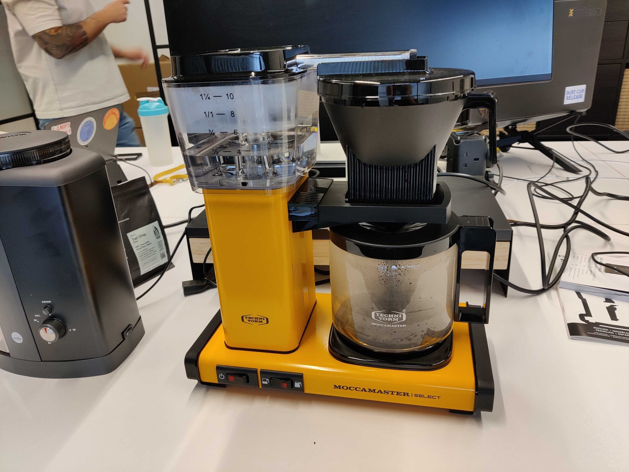 Photo of a yellow Moccamaster Select filter coffee machine sat on a desk in front of a computer monitor